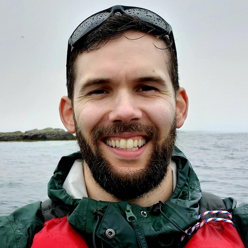 Evan wearing a green rain jacket with the ocean in the background